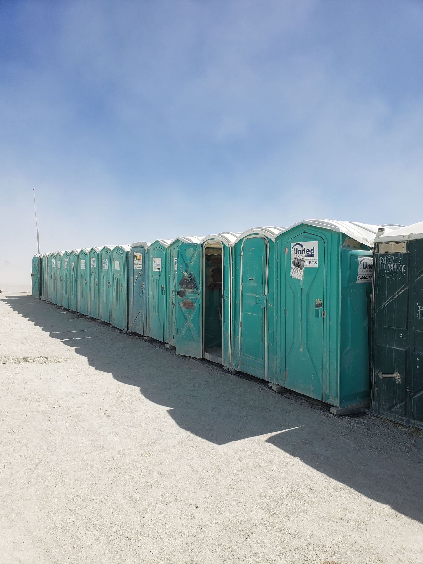 A row of portable toilets receding into dust on the playa.